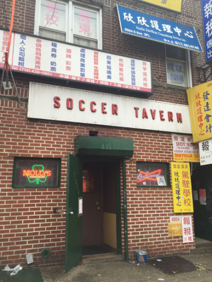 Just a red brick wall and a nondescript green door, flanked by two small windows with neon beer signs. 