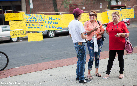 A member of Queens Neighborhood United engaging passers by about the questions and statements about police on the hand-made yellow signs in Spanish.
