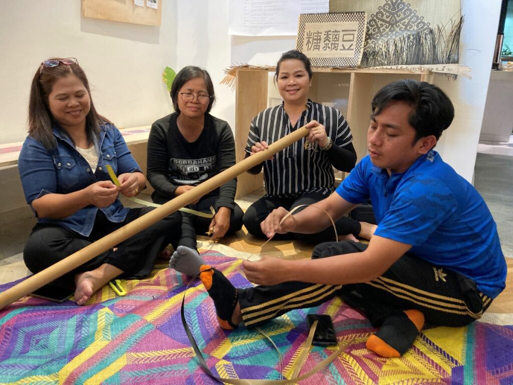 From left to right, Lili Naming, Siat Yanau, Johin Endelengau, and Shahrizan bin Juin, weavers from Keningau, Sabah explaining how the bamboo pus is processed for mat-weaving at Rumah Lukis, Kuala Lumpur in July 2023. Photo by Fiona Lee. 
